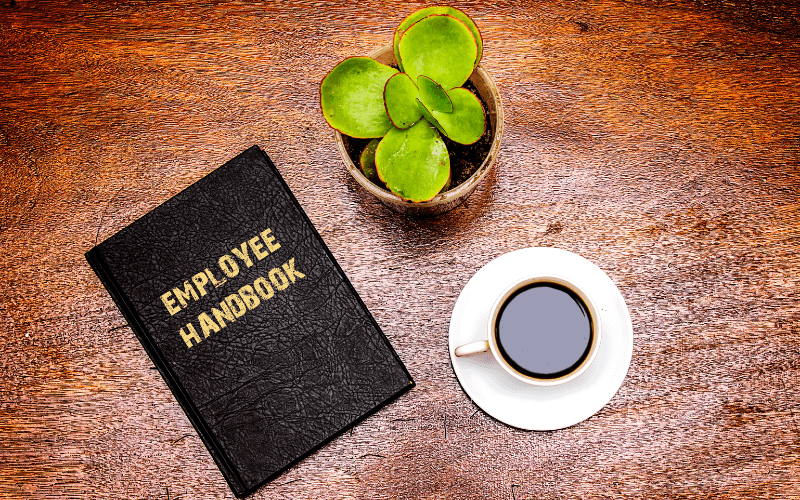 Employee handbook on table next to coffee